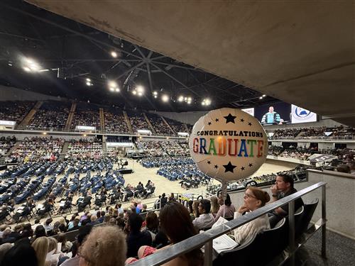 graduates on arena floor in background with COngratulations Graduate balloon in foreground
